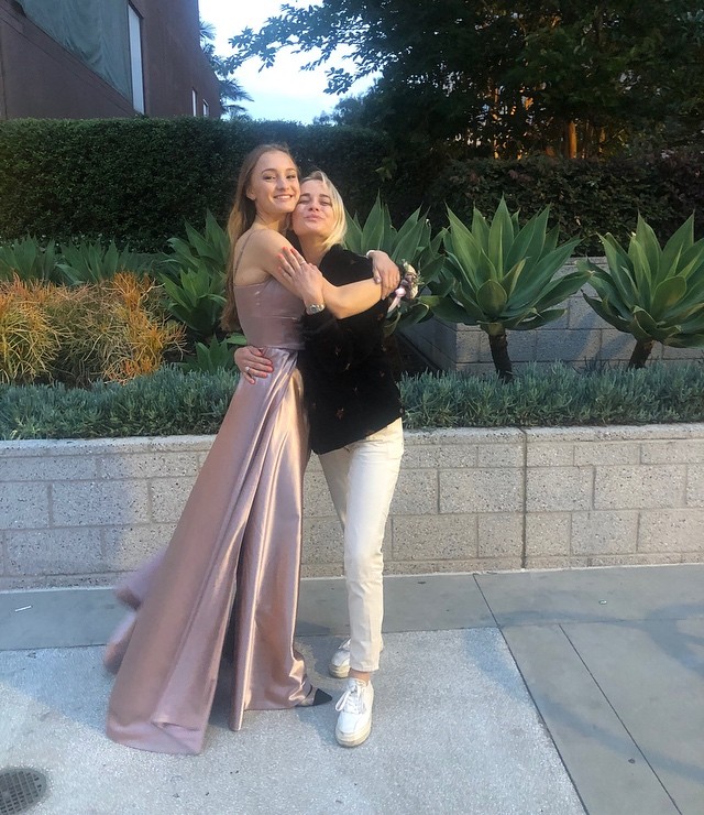 Ekaterina Gordeeva in a black outer and white pants posing with her sister in a light pink gown.